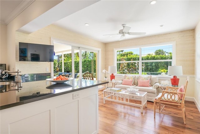 living room with a wealth of natural light, ceiling fan, crown molding, and light wood-style floors