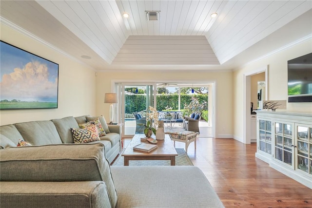 living room with wood finished floors, baseboards, visible vents, a tray ceiling, and ornamental molding