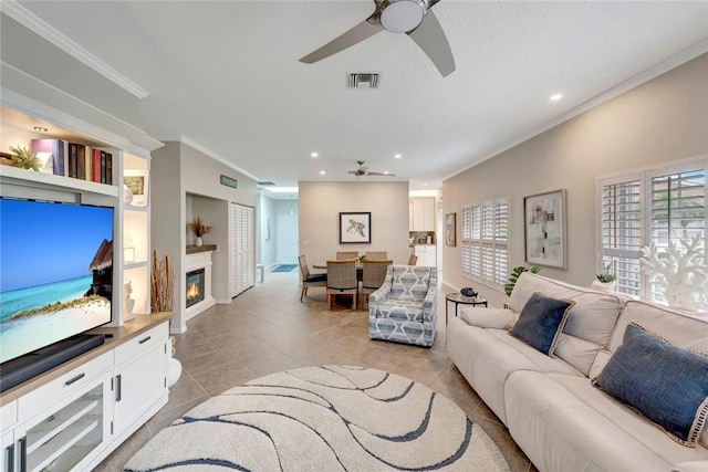 living room with ceiling fan, light tile patterned floors, visible vents, a glass covered fireplace, and crown molding