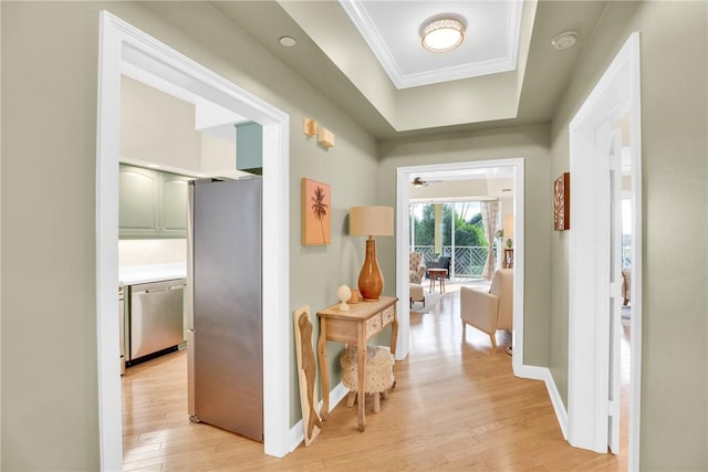 hall featuring ornamental molding, a tray ceiling, light wood-style flooring, and baseboards