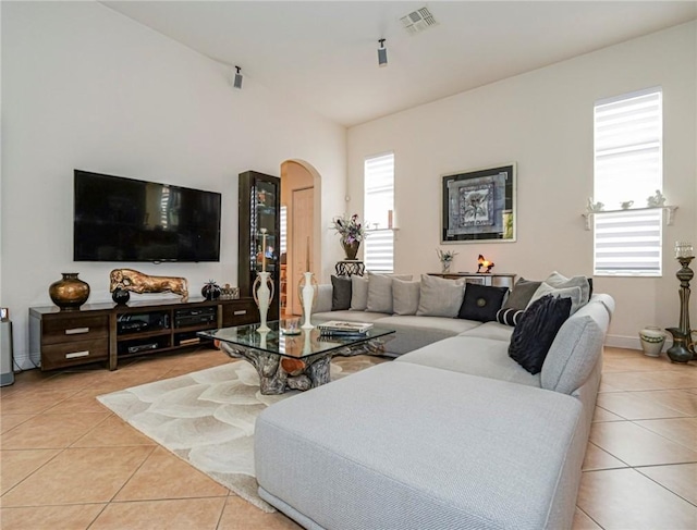 living area featuring light tile patterned floors, visible vents, arched walkways, and baseboards