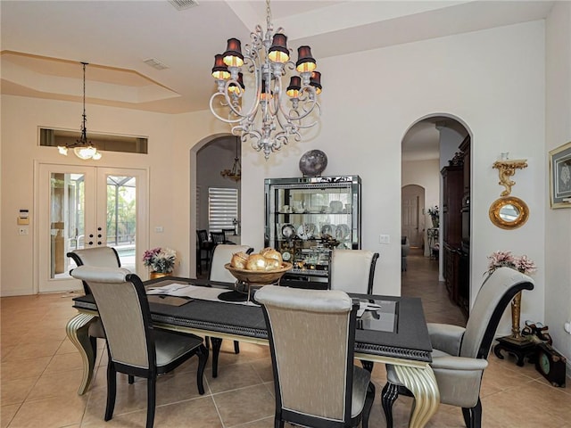 dining area featuring a tray ceiling, french doors, arched walkways, an inviting chandelier, and light tile patterned flooring