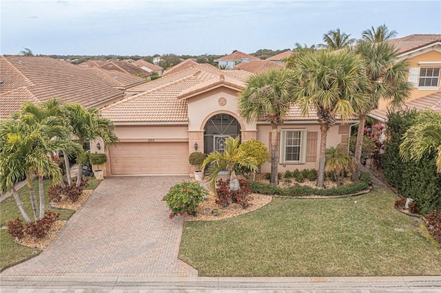 mediterranean / spanish home featuring a tile roof, an attached garage, decorative driveway, a front lawn, and stucco siding