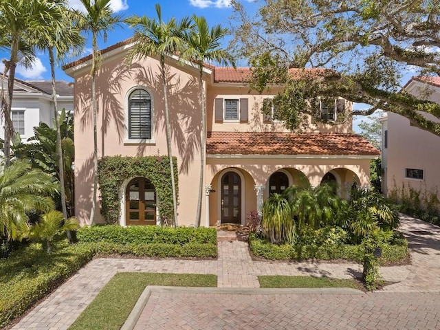 mediterranean / spanish-style home with french doors, a tiled roof, and stucco siding