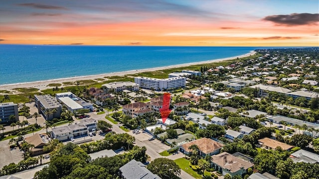 aerial view at dusk featuring a water view and a beach view