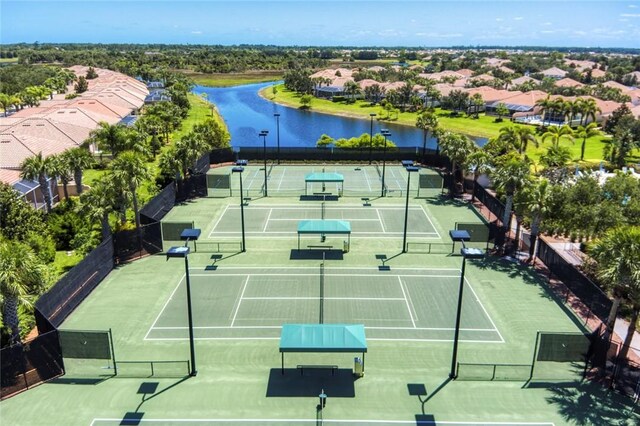 view of tennis court with a water view and fence
