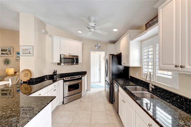 kitchen featuring appliances with stainless steel finishes, a sink, a ceiling fan, white cabinets, and dark stone counters
