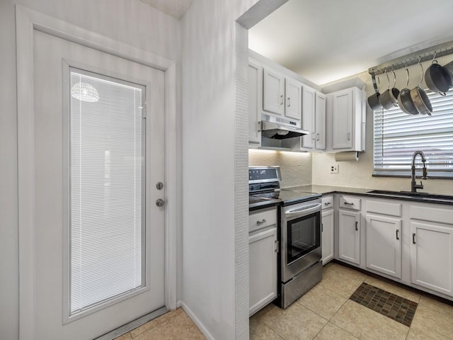 kitchen featuring stainless steel range with electric stovetop, a sink, under cabinet range hood, dark countertops, and white cabinets