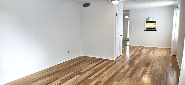 unfurnished room with baseboards, a textured ceiling, visible vents, and wood finished floors