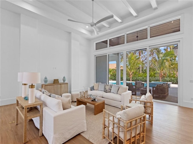 living area with beamed ceiling, a towering ceiling, ceiling fan, and wood finished floors