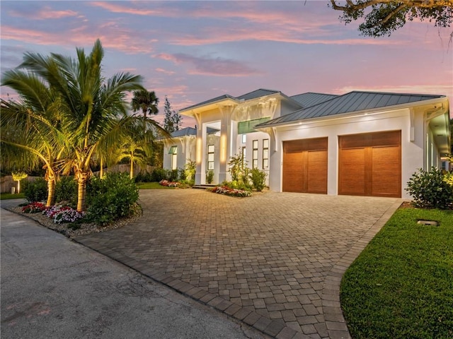 view of front of home with a garage, stucco siding, decorative driveway, and a standing seam roof