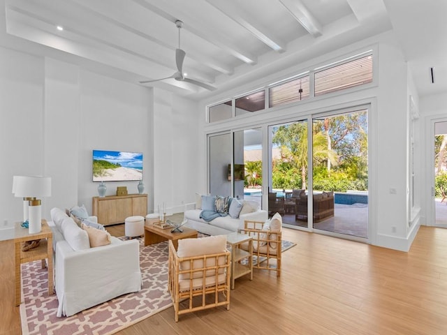living room with beamed ceiling, baseboards, a towering ceiling, wood finished floors, and a ceiling fan