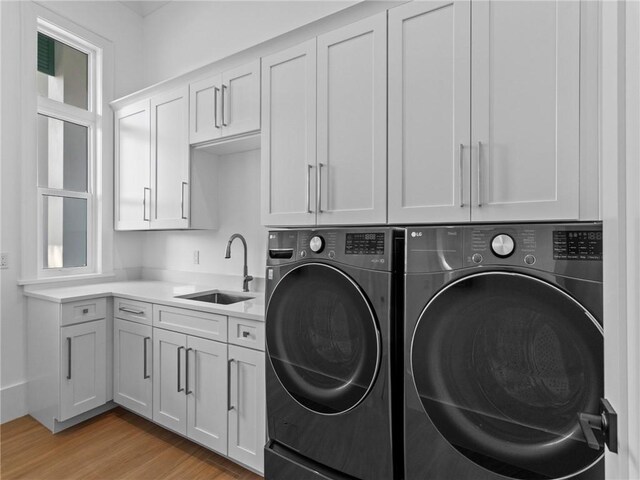 laundry area with light wood finished floors, washer and dryer, cabinet space, and a sink