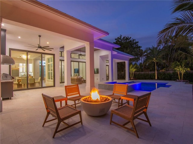 patio terrace at dusk with a ceiling fan, a fenced in pool, a fire pit, and exterior kitchen