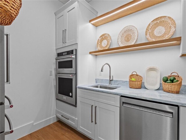 kitchen with light stone counters, a sink, open shelves, light wood finished floors, and stainless steel appliances