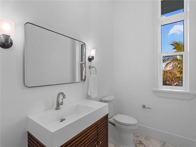 half bathroom featuring baseboards, toilet, and vanity