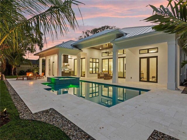 back of house at dusk with a patio area, a standing seam roof, french doors, outdoor lounge area, and metal roof