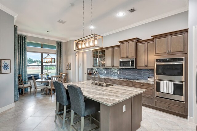 kitchen with crown molding, stainless steel appliances, hanging light fixtures, sink, and an island with sink