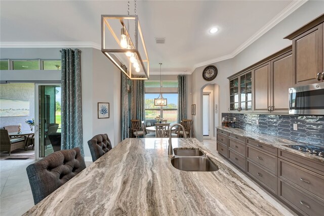 kitchen featuring stainless steel appliances, light stone counters, decorative backsplash, sink, and ornamental molding