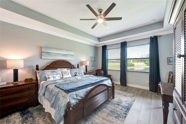 bedroom with light hardwood / wood-style flooring, ceiling fan, and a tray ceiling