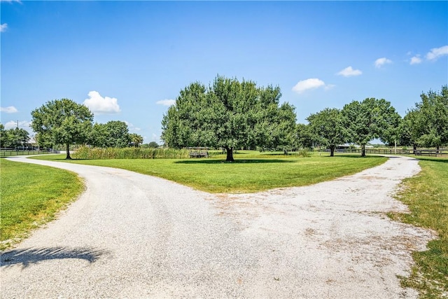 view of home's community with a yard, a rural view, gravel driveway, and fence