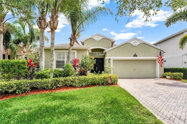 view of front facade with an attached garage, decorative driveway, stucco siding, and a front yard