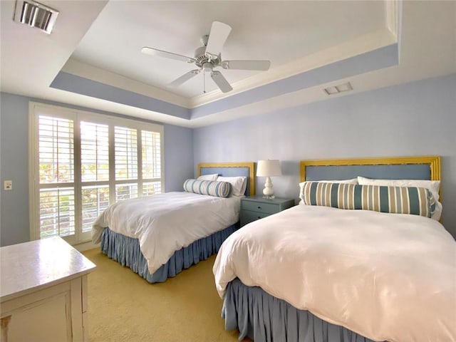 carpeted bedroom with ceiling fan and a tray ceiling