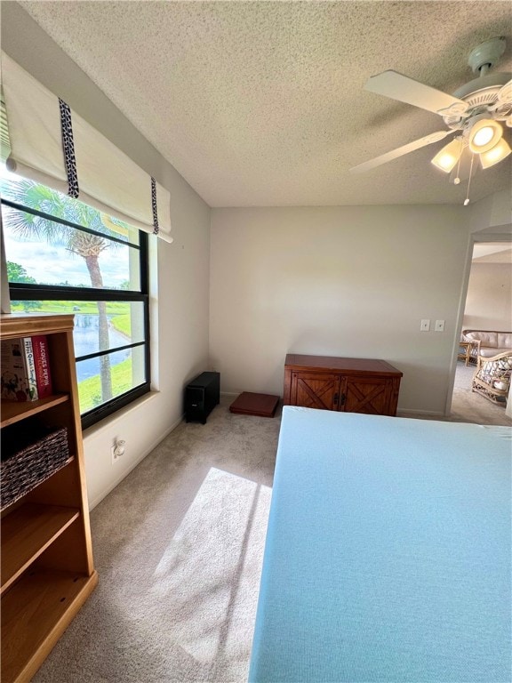 bedroom featuring a textured ceiling, light colored carpet, and ceiling fan