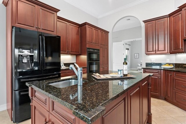 kitchen featuring sink, crown molding, an island with sink, dark stone counters, and black appliances