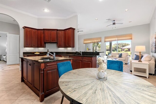 kitchen with sink, light tile patterned floors, dark stone counters, and a center island with sink