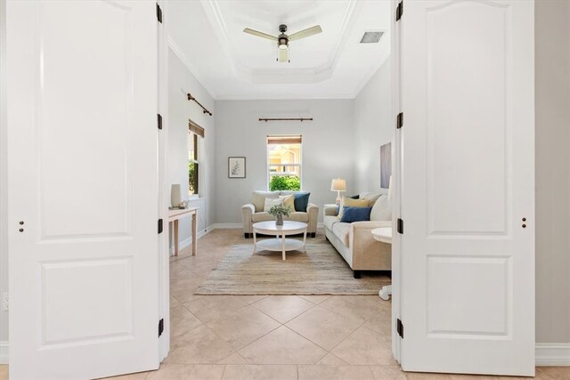 living room featuring ceiling fan, ornamental molding, light tile patterned floors, and a tray ceiling