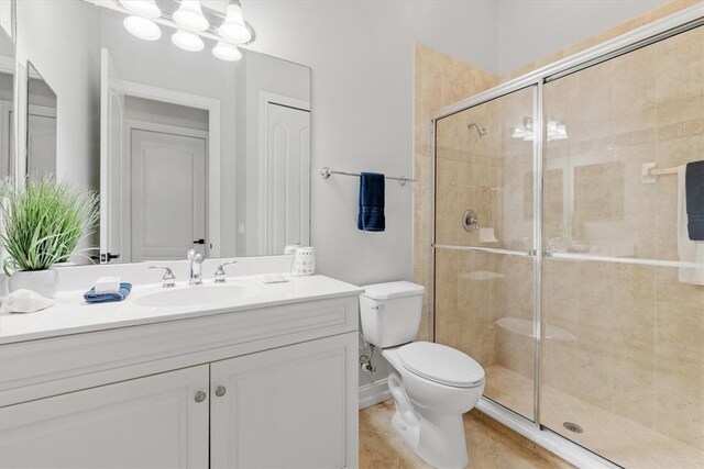 bathroom featuring tile patterned flooring, vanity, toilet, and a shower with door