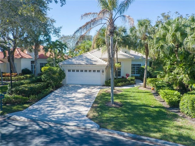 view of front of property with a garage, driveway, a tiled roof, stucco siding, and a front yard