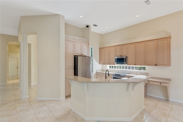 kitchen featuring appliances with stainless steel finishes, a kitchen island with sink, light brown cabinets, and a kitchen breakfast bar