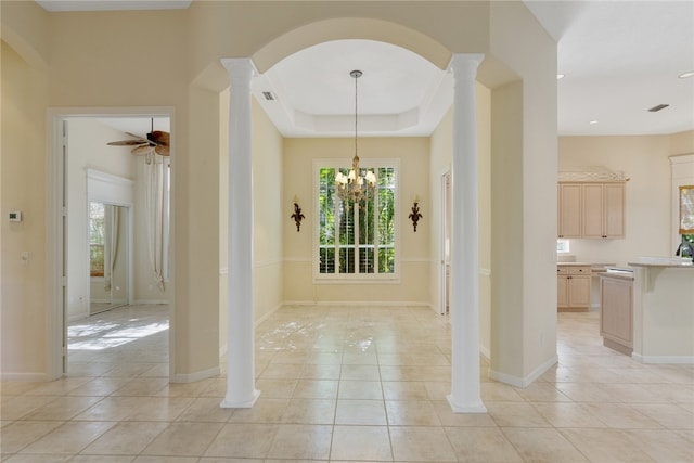 interior space featuring decorative columns, light tile patterned flooring, ceiling fan with notable chandelier, and a tray ceiling