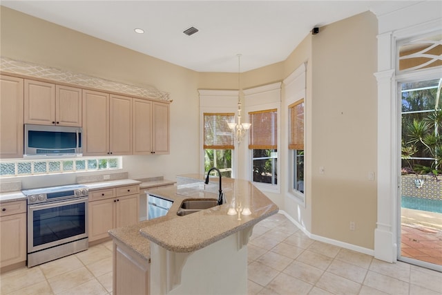 kitchen featuring sink, appliances with stainless steel finishes, an inviting chandelier, an island with sink, and a kitchen bar