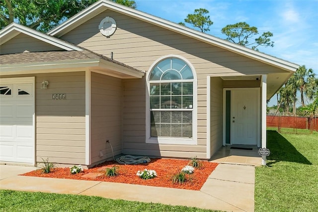 entrance to property featuring a garage, fence, a yard, and a shingled roof