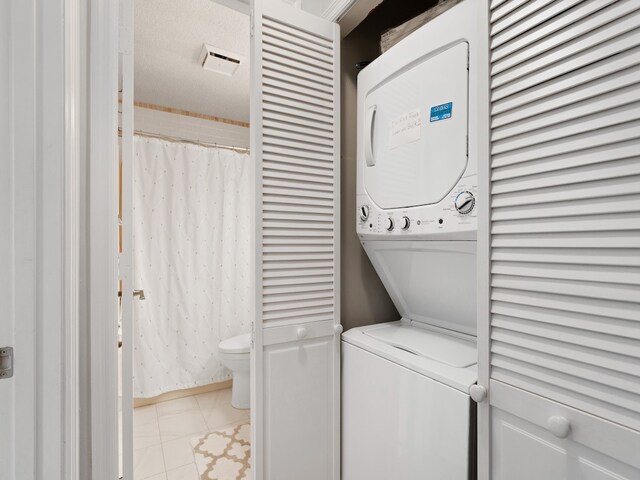 laundry area featuring a textured ceiling, stacked washer / dryer, and light tile patterned floors