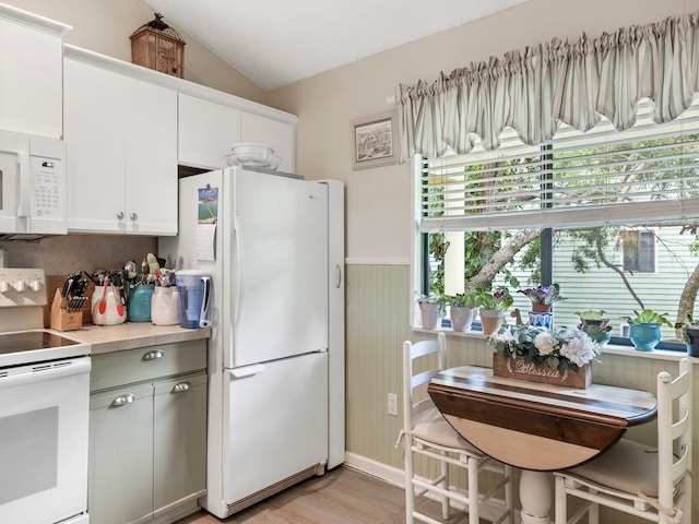 kitchen with white cabinetry, a textured ceiling, white appliances, light hardwood / wood-style flooring, and vaulted ceiling