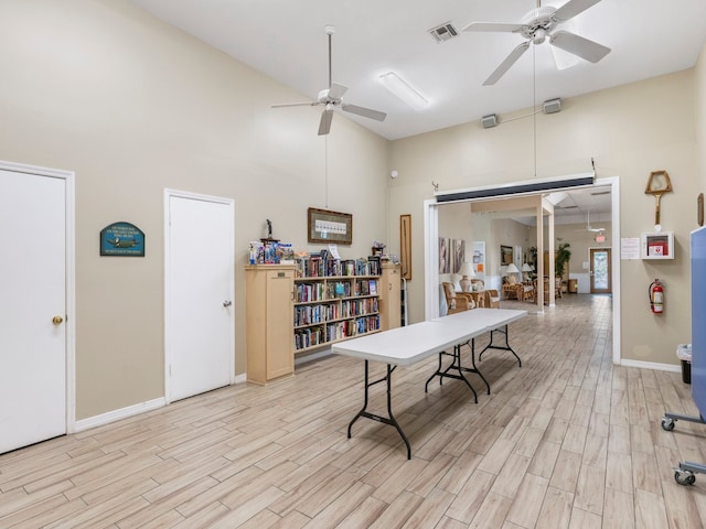 recreation room with a towering ceiling, ceiling fan, and light hardwood / wood-style flooring