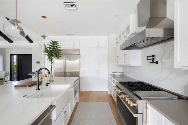 kitchen featuring built in appliances, wall chimney range hood, light wood-type flooring, and white cabinetry
