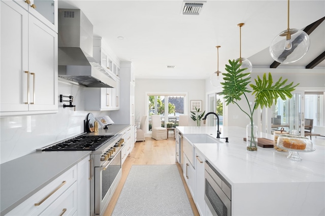 kitchen featuring stainless steel appliances, wall chimney range hood, light wood-style flooring, a sink, and white cabinets