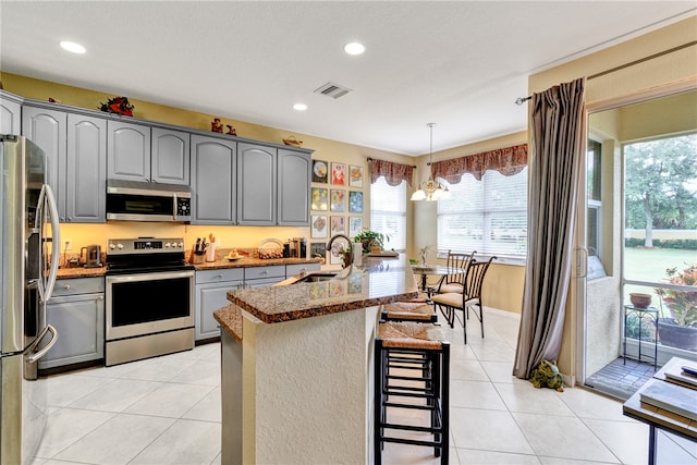 kitchen with gray cabinets, appliances with stainless steel finishes, sink, and a kitchen bar