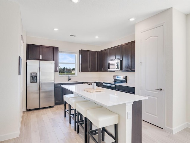 kitchen featuring sink, appliances with stainless steel finishes, a kitchen island, a kitchen bar, and dark brown cabinetry