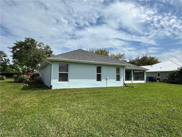 back of property featuring a shingled roof, a yard, a sunroom, and stucco siding