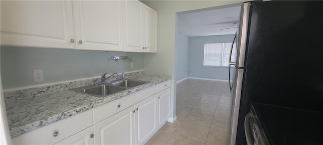 kitchen with sink, light tile patterned floors, light stone counters, white cabinetry, and stainless steel refrigerator