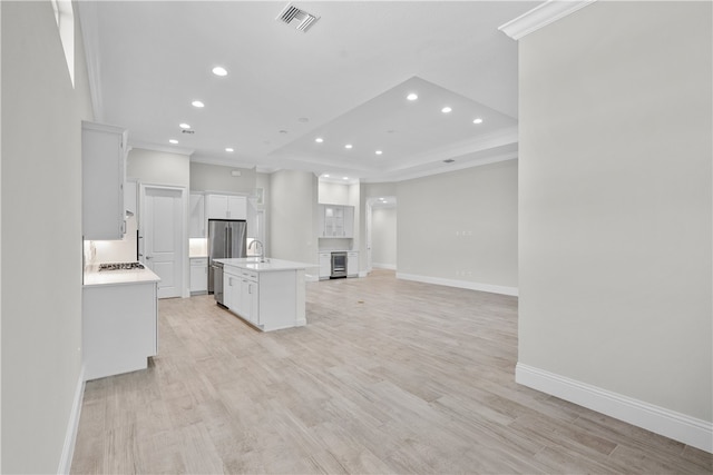 kitchen featuring a center island with sink, crown molding, light hardwood / wood-style floors, white cabinets, and a tray ceiling