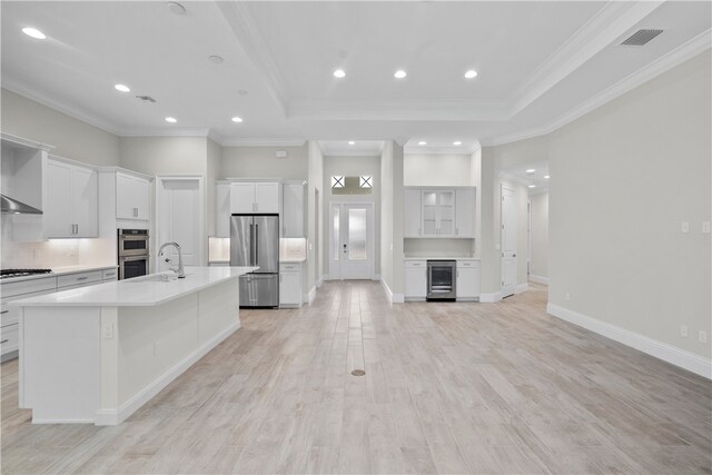 kitchen featuring stainless steel appliances, wine cooler, an island with sink, white cabinets, and light hardwood / wood-style flooring