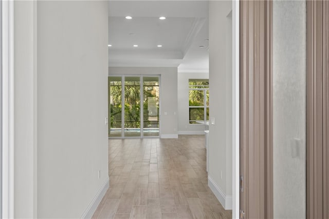 corridor with light wood-type flooring, crown molding, and a tray ceiling