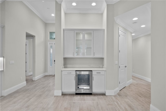 bar featuring ornamental molding, beverage cooler, light hardwood / wood-style floors, and white cabinets